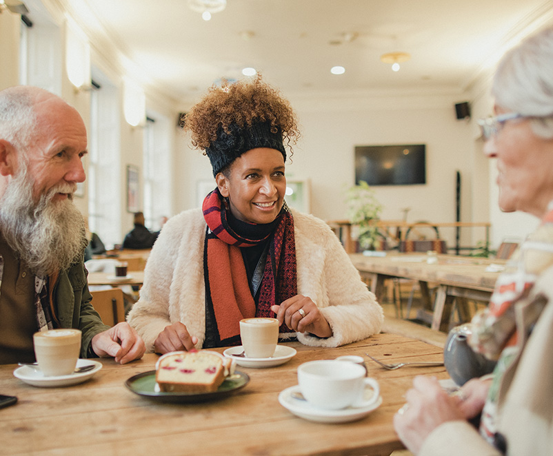Photo of 3 older adults enjoying a conversation around a table drinking tea